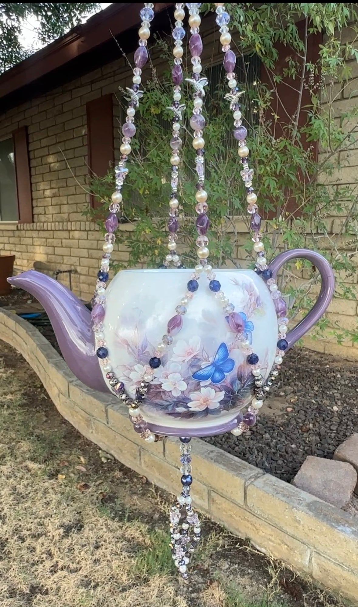 Decorative teapot with beaded chain against a brick wall and garden background