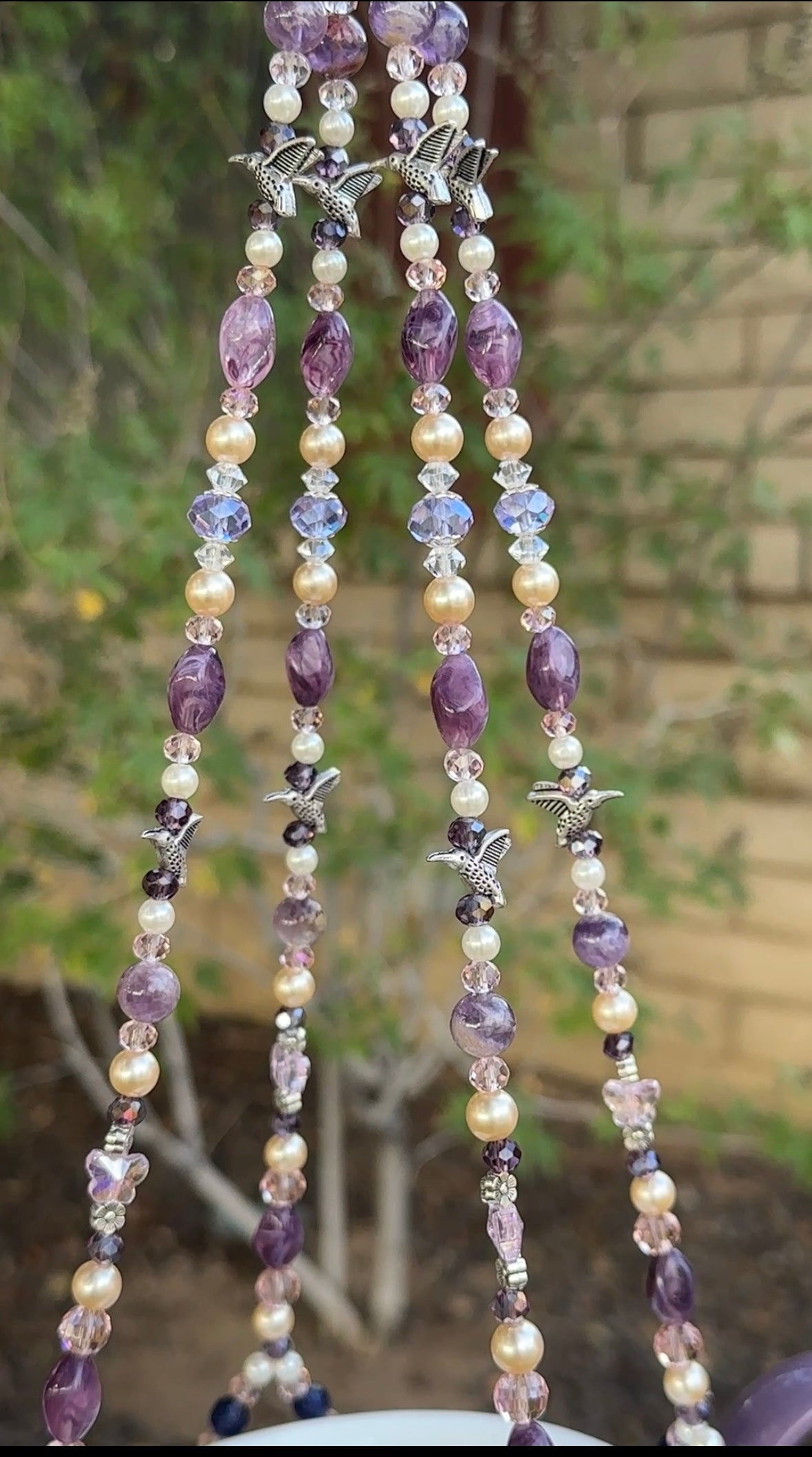 Jeweled string with purple, white, and clear crystals hanging against a blurred natural background.